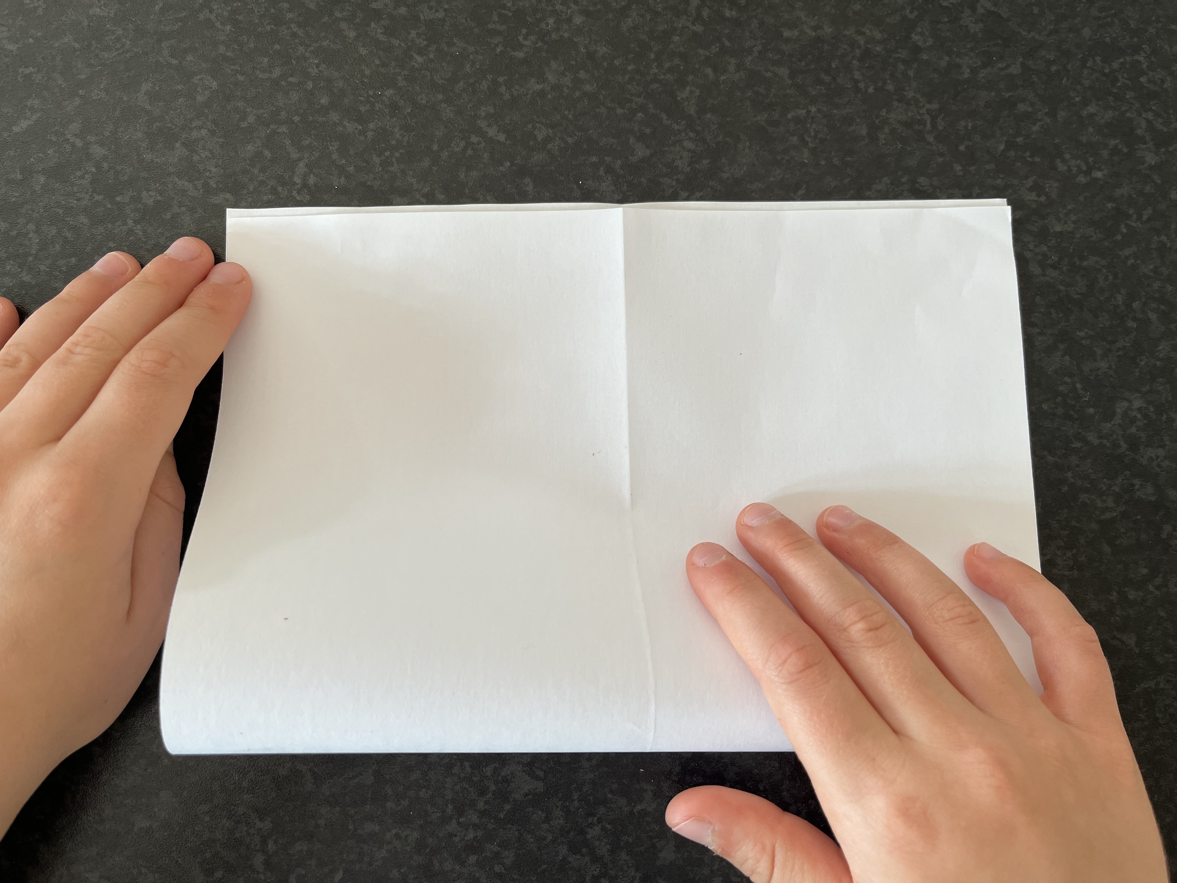 Trin 4: Fold papiret på midten igen, denne gang på tværs, så det bliver kortere og får form som en lille bog.